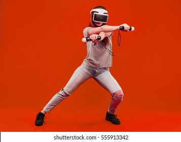 happy young woman in virtual reality helmet isolated on orange background jumping and smiling. VR glasses. - Shutterstock ID 555913342