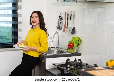 happy young woman washing dishes in the sink in the kitchen at home