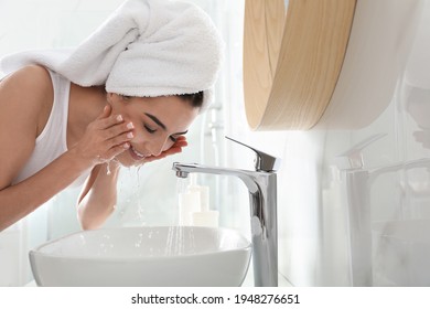 Happy young woman washing face in bathroom - Powered by Shutterstock