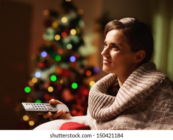 Happy Young Woman Watching Tv In Front Of Christmas Tree