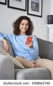 Happy Young Woman Watching Video Looking At Smartphone Relaxing On Couch, Smiling Hispanic Teen Girl Enjoying Using Online Mobile Apps For Education Or Entertainment On Cell Phone At Home.