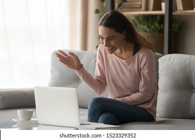 Happy young woman waving hand making distance video call online chat looking at laptop screen sit on sofa, smiling girl laughing talking to webcam communicate by internet computer pc app at home - Powered by Shutterstock