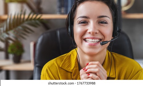Happy young woman wear headset communicating by conference call speak looking at computer at home office