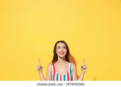 Happy young woman wear red blue swimsuit pointing fingers hands above on copy space mock up promo area isolated on vivid yellow color wall background studio. Summer hotel pool sea rest sun tan concept