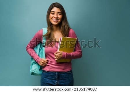 Happy young woman wearing a backpack while carrying books and notebooks to college