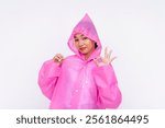 Happy young woman wearing a bright pink hooded raincoat demonstrates a cheerful gesture while making an ok sign. Isolated on a white background.