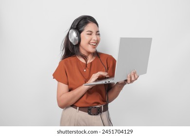 Happy young woman wearing brown shirt and headphone while holding laptop to listen music isolated over white background. - Powered by Shutterstock