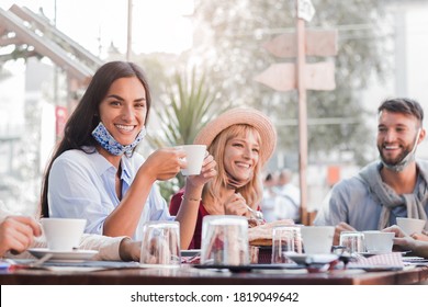 Happy Young Woman Wearing Face Mask Smiling At The Camera At The Restaurant Cafè. Group Of Multiracial Friends Having A Fun Conversation And Talking Together. New Normal Concept.