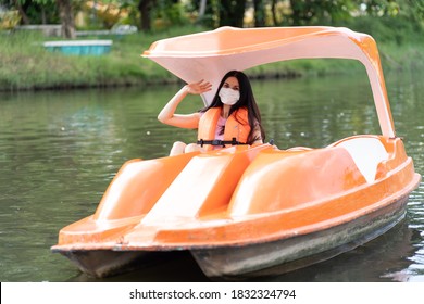 Happy Young Woman Wearing Face Mask, In Safe Life Jacket While Sitting On Pedal Boat On Water Park At The Amusement Theme Park. Tourist Enjoying On Summer Vacation. Tourism, People, Holiday Concept