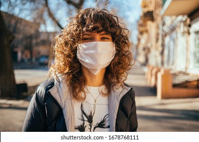 Happy Young Woman Wearing Facial Mask For Virus Protection Standing Outdoors On Sunny Spring Day.