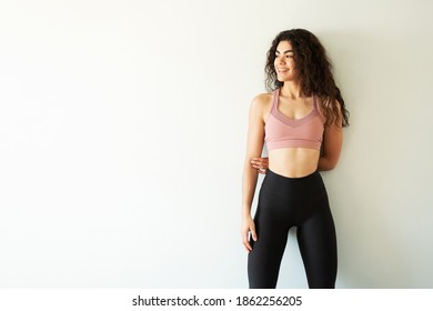 Happy Young Woman Wearing Leggings And Sportswear Looking To The Side And Smiling In A Solid Background. Copy Space Concept