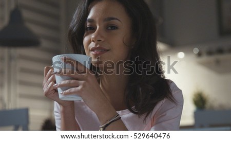 Happy young woman wearing pajama sitting with tea/chocolate/coffee mug, smiling.