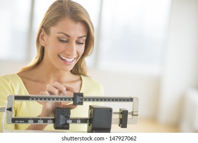 Happy Young Woman Weighing Herself On Balance Scale At Health Club