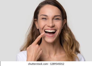 Happy young woman with white straight teeth perfect dent orthodontic smile pointing at tooth looking at camera isolated on studio blank background, dental health stomatology service concept, portrait