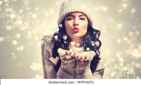 Happy Young Woman With Winter Clothes Blowing Snow And Hearts