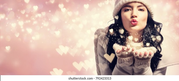 Happy young woman with winter clothes blowing snow and hearts