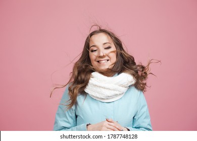 Happy Young Woman In A Winter Jacket And Scarf, Hair In The Wind. Portrait On A Pink Background