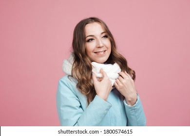 Happy Young Woman In A Winter Jacket And Scarf, Hair In The Wind. Portrait On A Pink Background