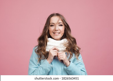 Happy Young Woman In A Winter Jacket And Scarf, Hair In The Wind. Portrait On A Pink Background