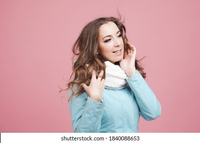 Happy Young Woman In A Winter Jacket And Scarf, Hair In The Wind. Portrait On A Pink Background