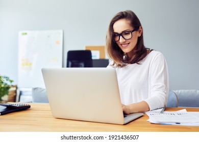 Fröhliche junge Frau, die zu Hause mit Laptop arbeitet