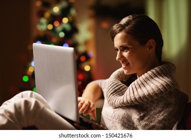 Happy Young Woman Working On Laptop In Front Of Christmas Tree