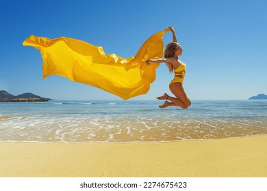 Happy young woman with a yellow light one Cloth jumping at sand beach. Relaxing, fun, and enjoy holiday at tropical paradise beach with blue sky. Girl in summer vacation.