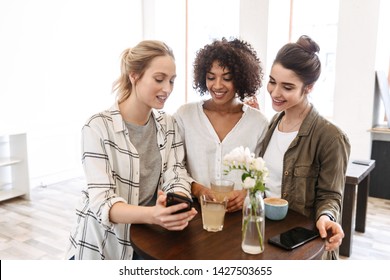 Happy young women friends having coffee break while relaxing at the cafe indoors, using mobile phone - Shutterstock ID 1427503655