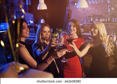 Happy young women with glasses of wine and cocktails enjoying a night out in stylish bar.