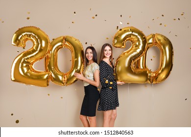 Happy Young Women With Golden 2020 Balloons On Beige Background. New Year Celebration