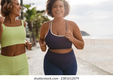 Happy young women jogging along the sunny ocean promenade in fitness clothing. Two female runners that represent body diversity enjoy a healthy, outdoor workout routine. - Powered by Shutterstock