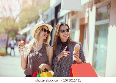 Happy young women with shopping bags and ice cream having fun on city street