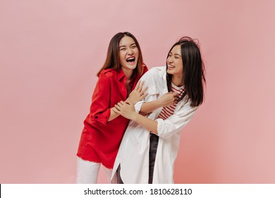 Happy young women in trendy oversized shirts laugh on isolated. Brunette Asian girls in stylish outfits smile and have fun on pink background.