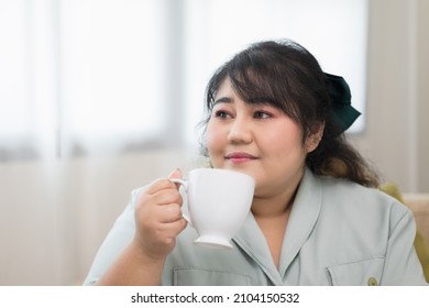 Happy young women's plus sitting on sofa drinking coffee in living room at home. Body positive plus size female lives happily and is proud of herself. - Powered by Shutterstock