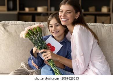 Happy Younger Mom And Kid Celebrating Mothers Day, Birthday, 8 March Together. Grateful Mom Receiving Gifts, Flowers Bunch, Handmade Greeting Card From Preteen Son, Hugging Child With Love