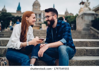 Fröhliches jugendliches Paar, das sich ansieht und lächelt, während es auf einer Treppe vor der Universität sitzt und sich nach dem Studium ausruht