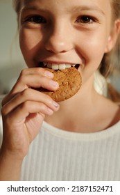 Happy Youthful Girl Biting Fresh Tasty Homemade Cookie Of Round Shape While Standing In Front Of Camera And Looking At You