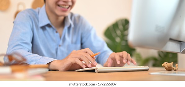 Happyman works with a computer while sitting at the wooden working desk.