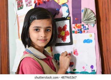 Happy/smiling Indian School Girl/kid/student Learning/drawing/decorating Pin Board In Her Art Class Room, Wearing Pink And Beige Uniform Kerala, India. Green Desk/table. Education Of Asian Girl Child.