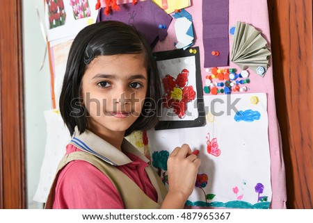 Happy/smiling Indian school girl/kid/student learning/drawing/decorating pin board in her art class room, wearing pink and beige uniform Kerala, India. green desk/table. Education of Asian girl child.