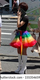 Harajuku, Tokyo/Japan- May8, 2016: A Woman In A Rainbow Skirt, White Boots And A Black Skirt, Holding A Rainbow Umbrella Talks On A Street Corner In Tokyo, Japan.