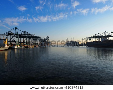 Harbor cranes unloading containers from ships on a sunny morning in the port of Antwerp.