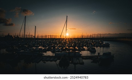 A harbor at sunset with sailboats anchored on calm waters, the sky painted in shades of yellow, orange and blue. - Powered by Shutterstock