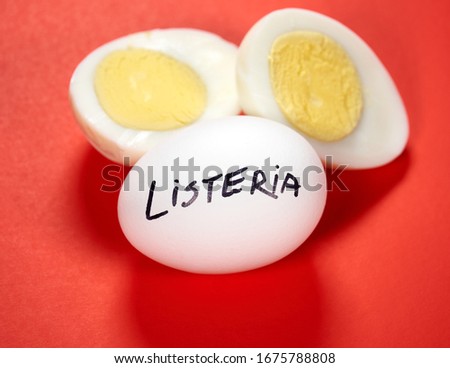 Hard boiled egg with Listeria writing on egg over red background. Listeriosis is a food-borne infection caused by Listeria bacteria. Listeria is caused by bacteria that can grow at cold temperatures