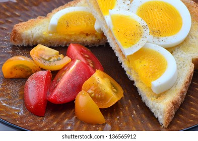 Hard Boiled Egg Slices On White Toast And Cherry Tomatoes Sprinkled With Salt And Pepper