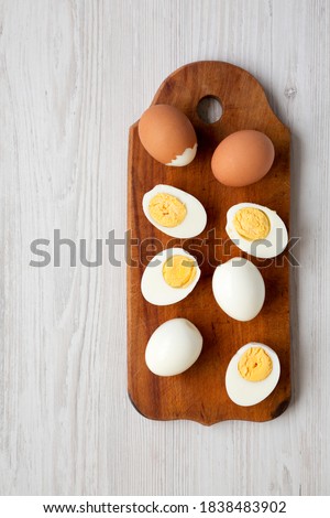 Hard Boiled Eggs on a rustic wooden board on a white wooden table, top view. Flat lay, overhead, from above. Copy space.
