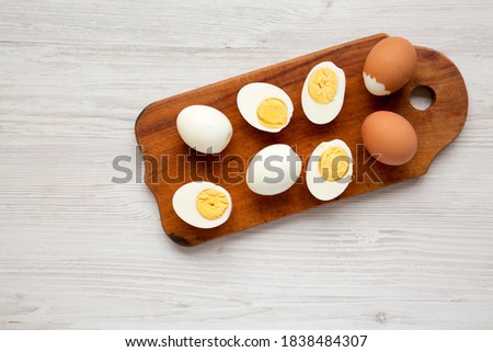 Hard Boiled Eggs on a rustic wooden board on a white wooden background, top view. Flat lay, overhead, from above. Copy space.