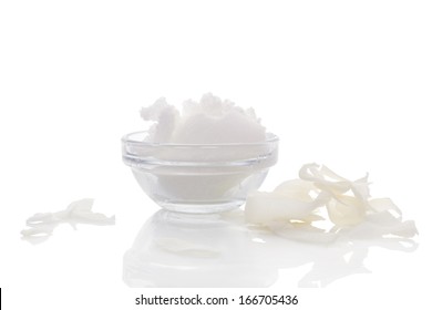 Hard coconut oil in glass bowl, dried coconut flakes on white background with reflection. Culinary healthy coconut oil background. Healthy cooking and bodycare still life.