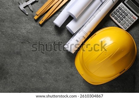 Hard hat, different engineering drawings, folding ruler, calculator and vernier caliper on grey table, flat lay. Space for text