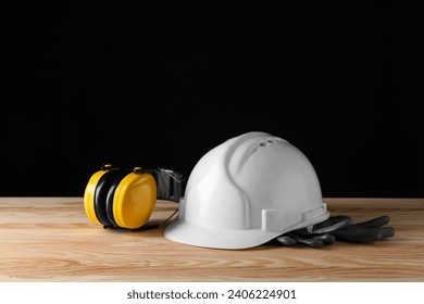 Hard hat, earmuffs and gloves on wooden table, space for text. Safety equipment